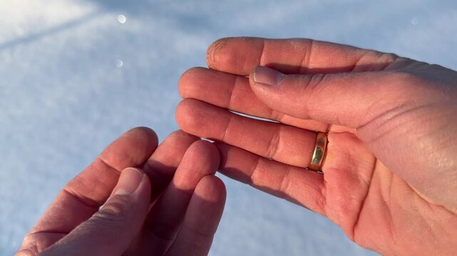 Rubbing Hands Together to Warm Up in Winter. POV close-up of two hands rubbing together to generate heat in cold snowy environment. Sun sparkles on snow in background.