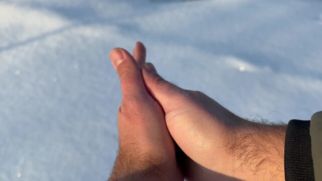 Rubbing Cold Hands Together in Winter Sunlight. POV shot of person rubbing bare hands together to generate warmth in cold snowy environment. Sun creates lens flares against white winter background.