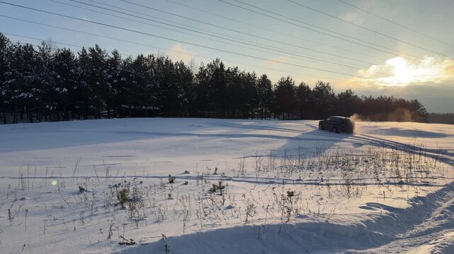Car Drifting in Deep Snow Near Winter Forest. Wide shot of black car performing drift in snow-covered field during golden hour. Snow sprays up from wheels as vehicle maneuvers near pine forest.