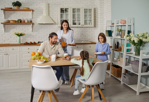 Happy parents and children enjoy quiet family brunch or breakfast in kitchen on day off. Mom, dad and kids gather to eat together around table in cozy kitchenette area interior in their studio flat 