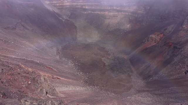 Aerial drone footage moving slowly forward over a large volcanic crater at Piton de la Fournaise on Reunion Island. Low clouds and mist drift across the crater,creating an atmospheric geological scene