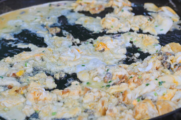 Thai crispy oyster omelet cooking on a large flat griddle.