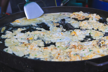 Thai crispy oyster omelet cooking on a large flat griddle.