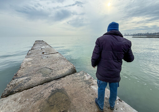 Man in winter clothing on a concrete pier overlooking the sea of Azov, Donetsk Oblast, Mariupol, Ukraine