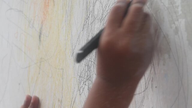 A small child's hand is scribbling on a white wall with a crayon.