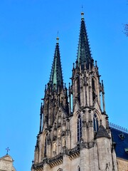 Fototapeta premium Saint Wenceslas Cathedral in Olomouc, Czech Republic, features two prominent Gothic spires with intricate stone carvings and pointed arches. The spires are topped with small golden finials. 