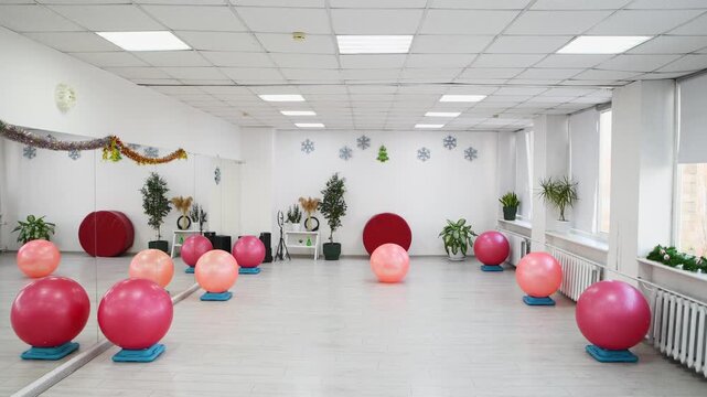 Bright fitness studio with pink and red exercise balls rolling to center on light floor