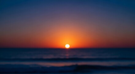 Fototapeta premium Blurry sunset over the ocean with a vibrant orange sun disc near the horizon and a sky transitioning from deep blue to warm orange