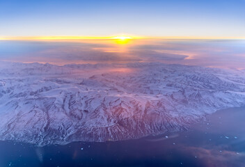 Aerial sunrise over snow covered coastal mountains in Greenland © Thomas