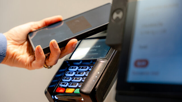 Woman using mobile phone to pay at supermarket checkout