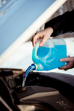 Pouring winter washer liquid into car engine compartment