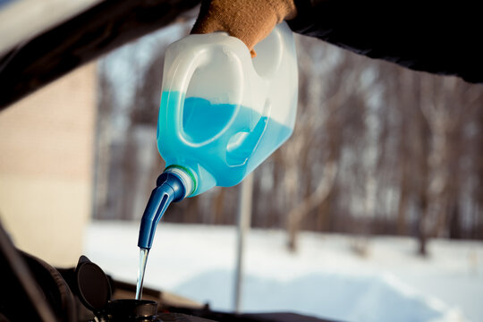 Pouring winter washer liquid into car engine