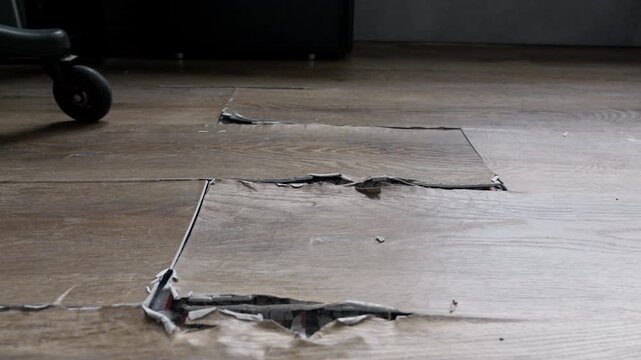 buckled laminate floor with torn planks and visible crack caused by heated floor expansion. closeup of damaged floor covering with lifted edges on which stands an office chair on wheels