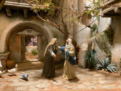 Biblical miniature scene of Mary and Elizabeth meeting in an ancient stone village courtyard with birds and plants, evoking faith, tradition, and Middle Eastern heritage.