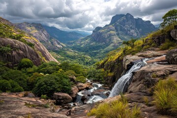 Naklejka premium Scenic vista of waterfall cascading into a lush valley, surrounded by towering mountains