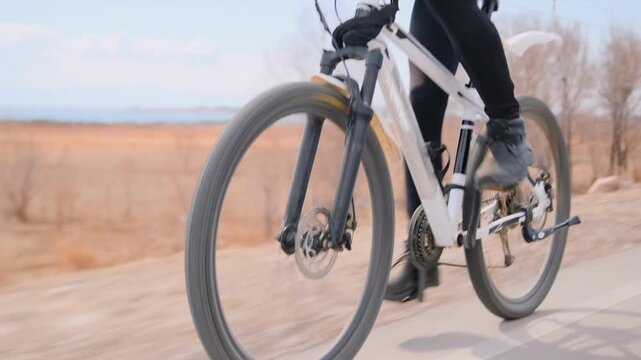 Fast male cyclist riding bicycle in open field, intense winter training on rural road through vast grasslands, endurance workout, outdoor fitness, solo athlete practicing long-distance cycling.