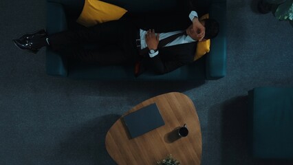 Top down aerial view of stressful boss look at decrease sales from laptop and lies on sofa. Tired manager working laptop while feeling stress. Skilled businessman having headache at work. Directorate. © InfiniteFlow