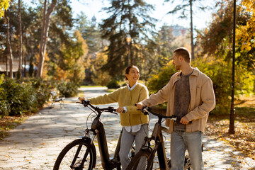 Obraz premium Couple enjoys a sunny afternoon ride in the park with electric bikes