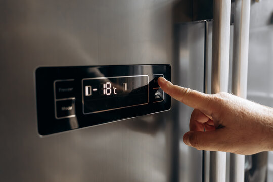 Hand adjusting temperature settings on modern refrigerator control panel, digital display showing negative temperature in Celsius