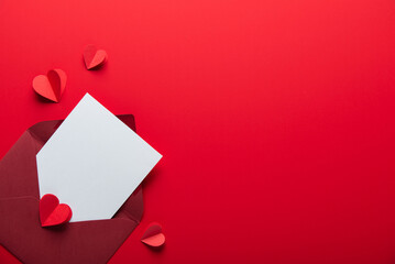 Love letter envelope with red paper craft hearts on red background. White paper with space for...