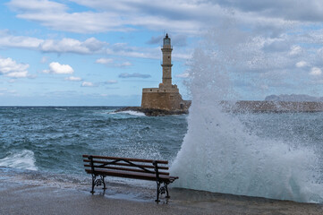 Wave crashing over seaside bench with Chania lighthouse in background