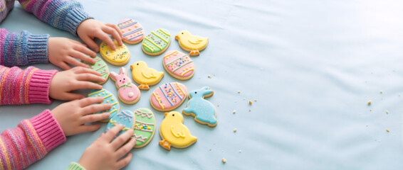 Children reaching for colorful Easter cookies on a blue background. Kids hands with bunny and egg shaped sugar biscuits. Festive holiday treats with copy space