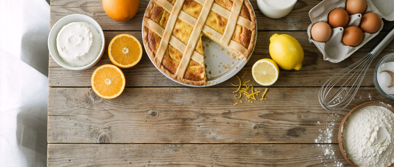 Top view of traditional Italian Easter ricotta pie on a rustic wooden table. Pastiera Napoletana with baking ingredients and copy space. Homemade festive dessert flat lay