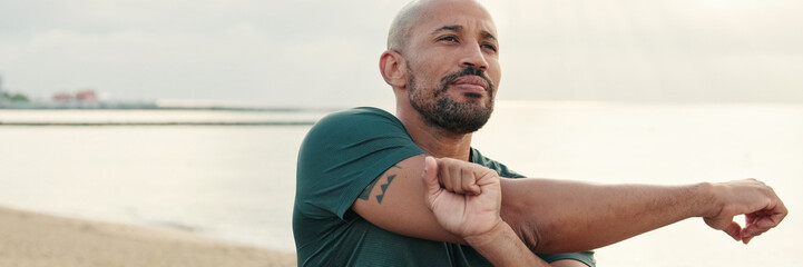 Fit guy does street workout, stretching and warming up against the sea on a cloudy day, sport...