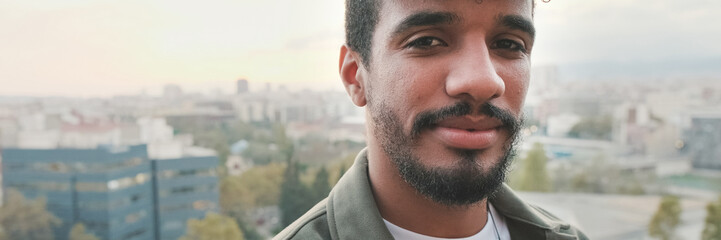Obraz premium Close-up of smiling young guy posing at the camera while standing on the balcony. Panoramic
