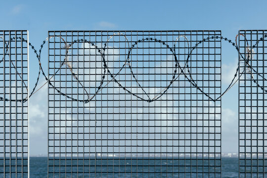 Security fence with barbed wire and ocean background