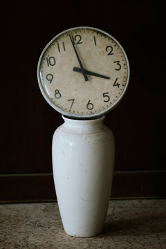 Old clock against dark backdrop on ceramic vase