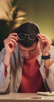 Burnout, stress and thinking with designer man in office at night for eye strain or fatigue. Brain fog, glasses and headache with employee at desk in dark design workplace for pressure or tension