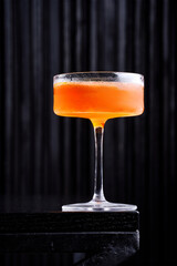 Elegant orange cocktail in a chilled coupe glass on a dark minimalist background.