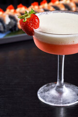 Gourmet sushi rolls topped with caviar and shrimp served with an orange cocktail on a dark background.