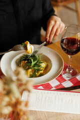 Young woman eating tortellini pasta ravioli with fork. red wine beside. close-up hi-res © Anton