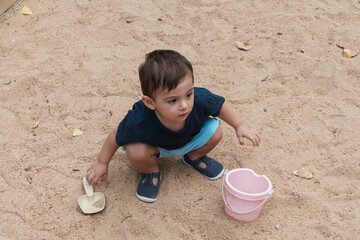 Toddler boy playing in sand with shovel and bucket