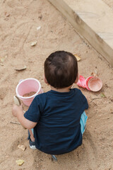 Toddler boy playing in sand with toy bucket outdoors