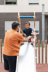 Father helping toddler son playing on slide