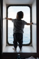 Baby watching ocean from ship porthole window
