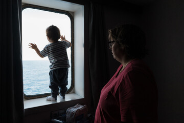 Child looking out ship porthole at vast sea
