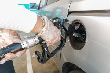 Person refueling car at gas station wearing gloves for hygiene