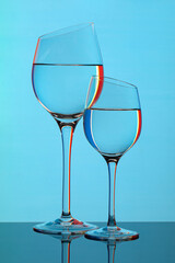 Two glass glasses filled with liquid with colored highlights on a blue background