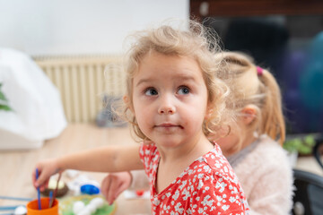 Fototapeta premium Young child paints at a table with bright colors in a room with friendly atmosphere during daytime