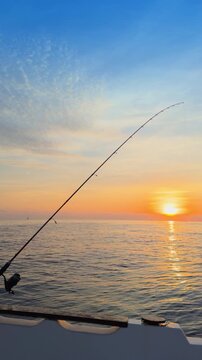 Offshore bottom fishing at sunset from boat with rod over calm sea