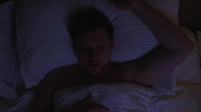 Top down view of frightened man suddenly waking up from horrible nightmare or sleep paralysis, feeling scared and anxious while lying in bed at night, suffering from sleep paralysis or panic attack