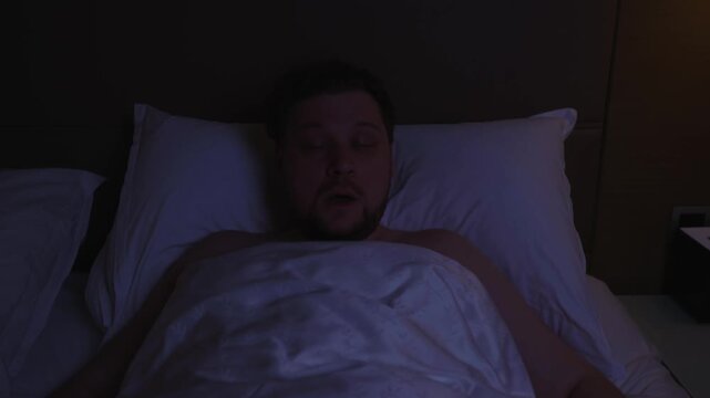 Agitated man suddenly waking up in his bed after having nightmare, feeling scared and restless from the bad dream, suffering from insomnia and sleep deprivation in a dark bedroom