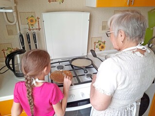A granddaughter helps her grandmother make pancakes in the kitchen.