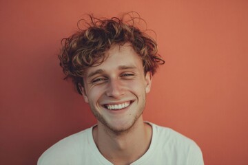Fototapeta premium Joyful young man smiling against a warm orange wall during a bright sunny day in the city, radiating happiness and positivity in a vibrant environment