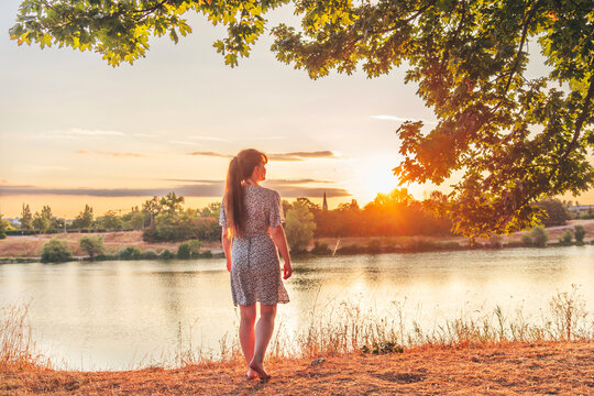 Young woman standing still near water during sunrise, enjoying quiet reflective moment outdoors. Concept of mental clarity, emotional balance and peaceful start of day