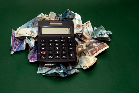 A calculator surrounded by crumpled Colombian pesos symbolizes debt, expenses, and financial stress.